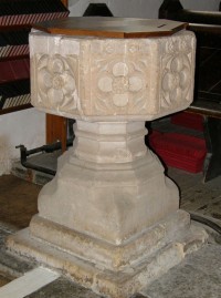 An octagonal stone font with floral carvings on the sides